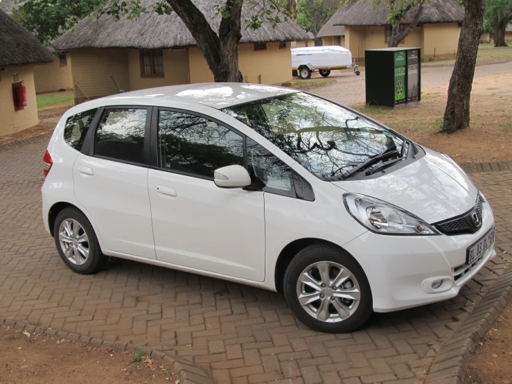 a white honda fit is parked on a brick patio