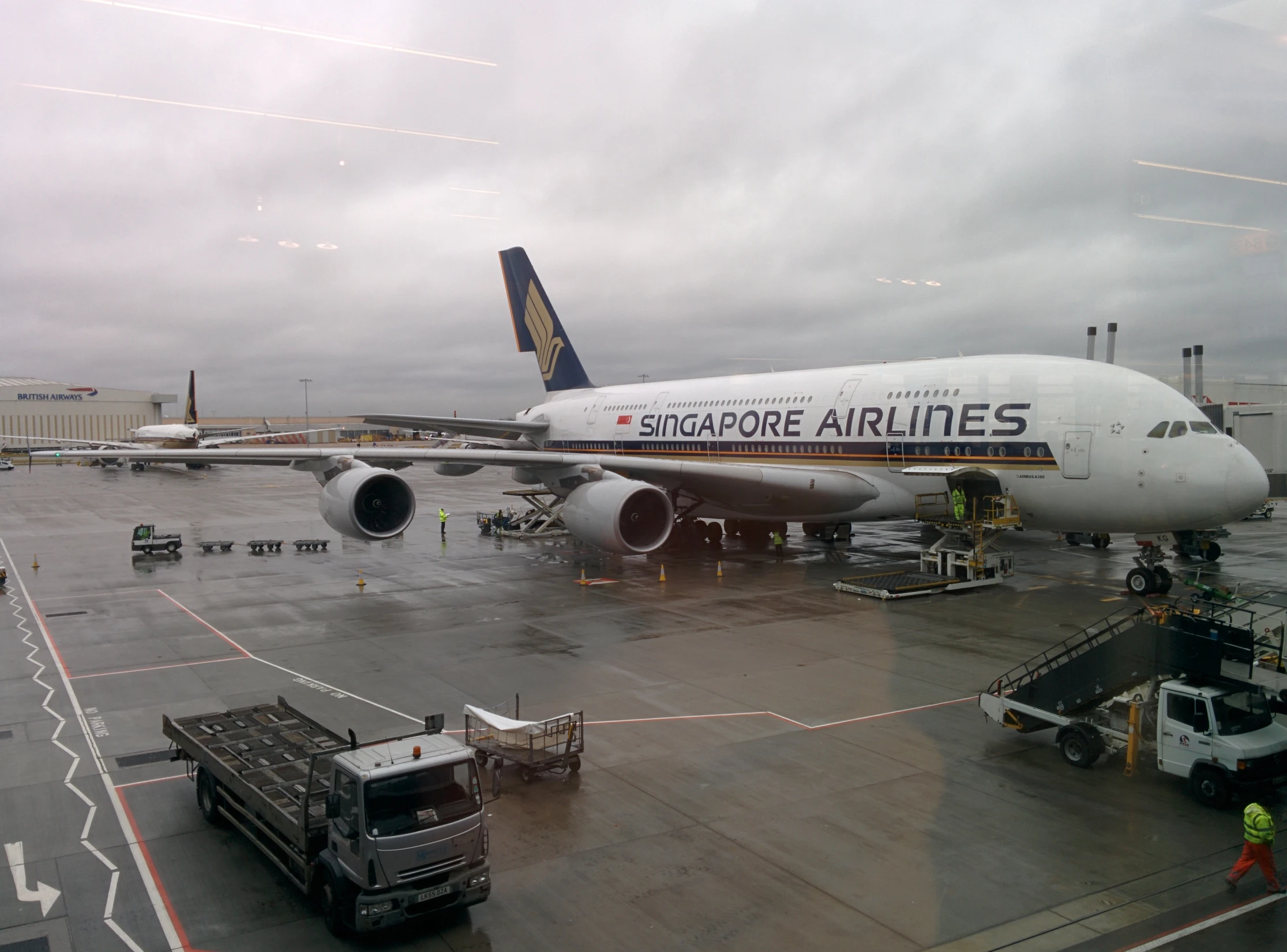 an airplane parked at the tarmac with a luggage cart and truck nearby