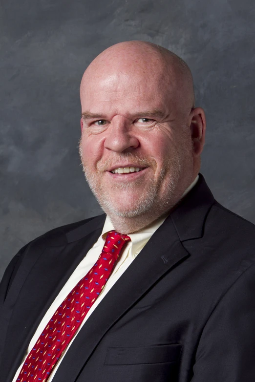 a smiling man wearing a suit and red tie