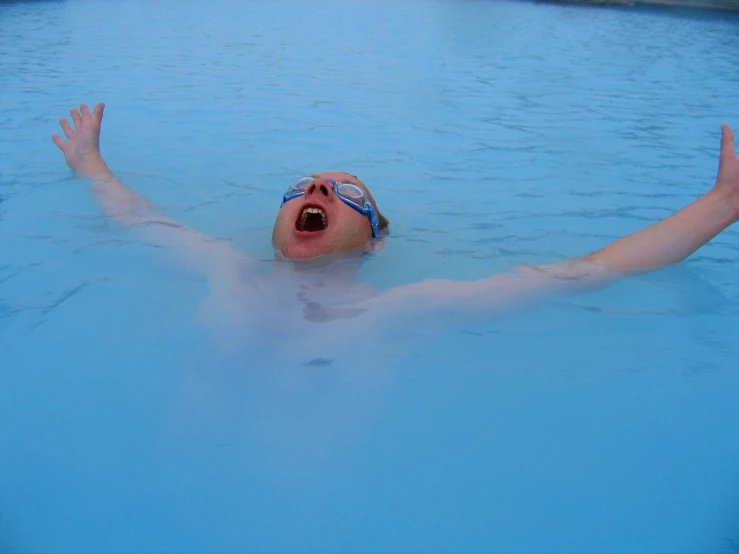 the man is swimming in the pool and making a silly face