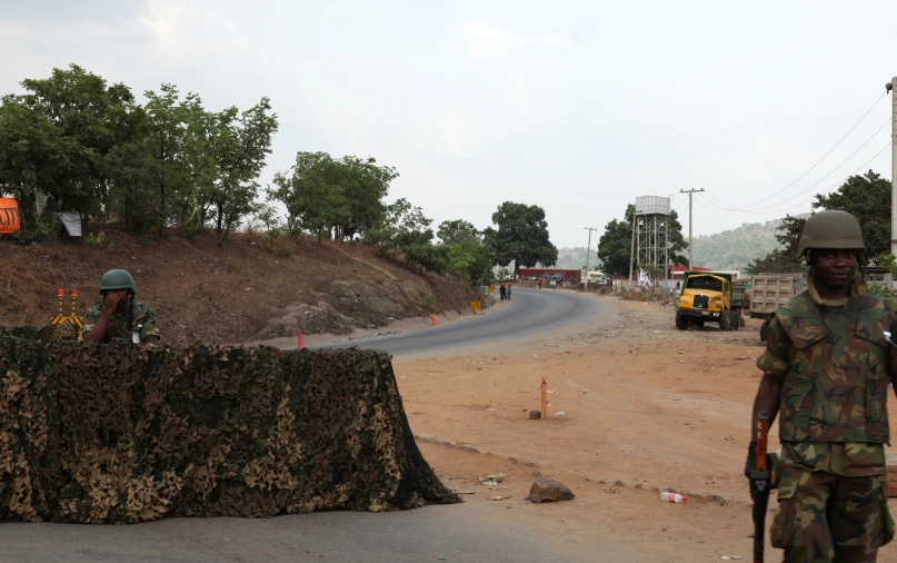 two soldiers walk by some construction equipment and trucks