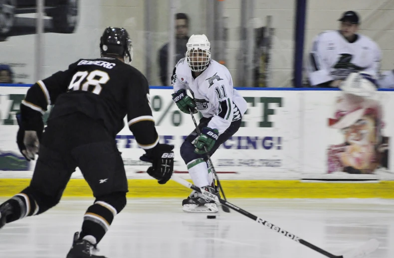 two men on opposite teams playing hockey, while a man in black is behind them