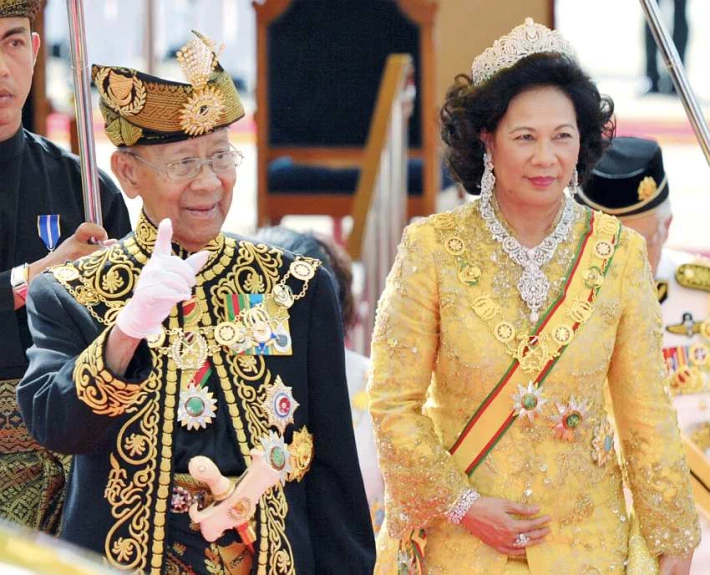 a queen wearing a crown walks next to an older man