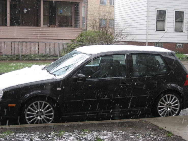 black car is parked on the corner while snow is falling