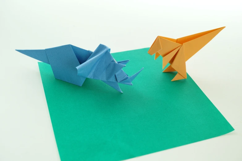 two small paper cranes in blue and orange on a green background