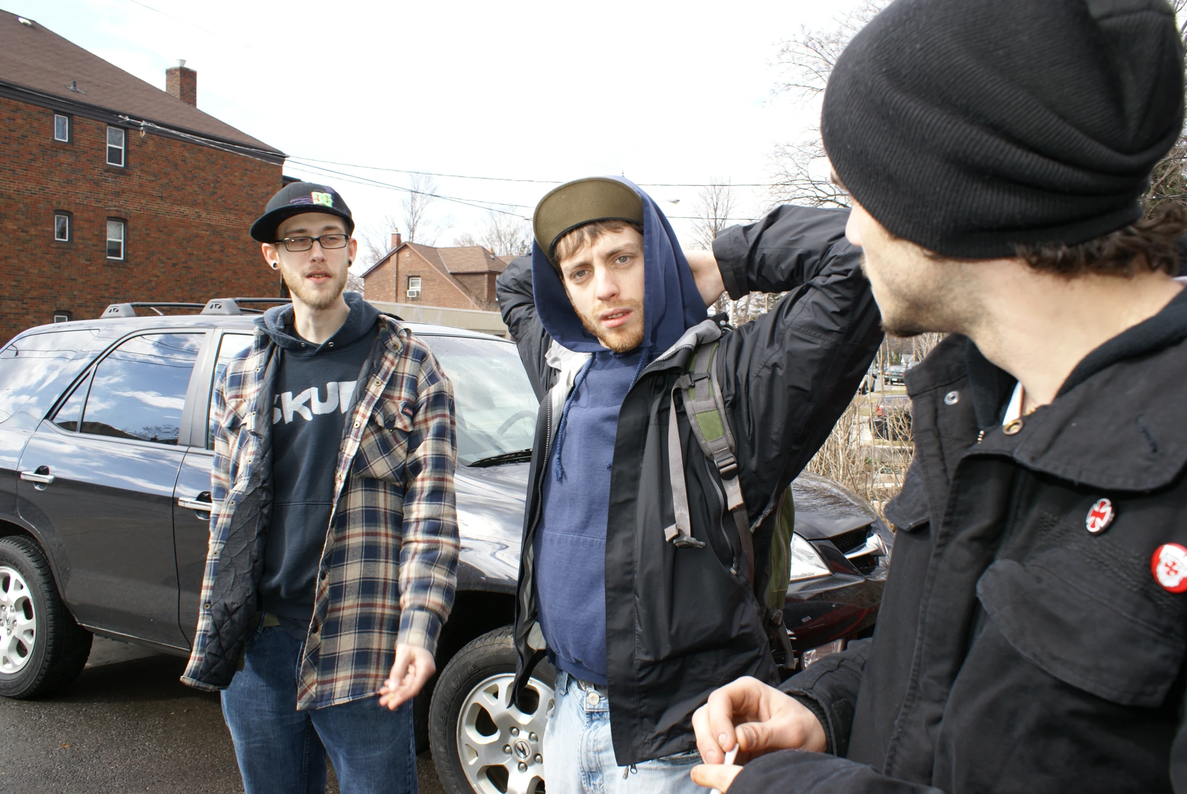 a man wearing a black jacket with a hoodie and jeans standing next to another man