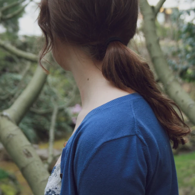 a woman with long hair in a ponytail with trees around her