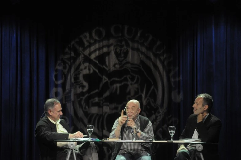 three men sitting around a table holding microphones