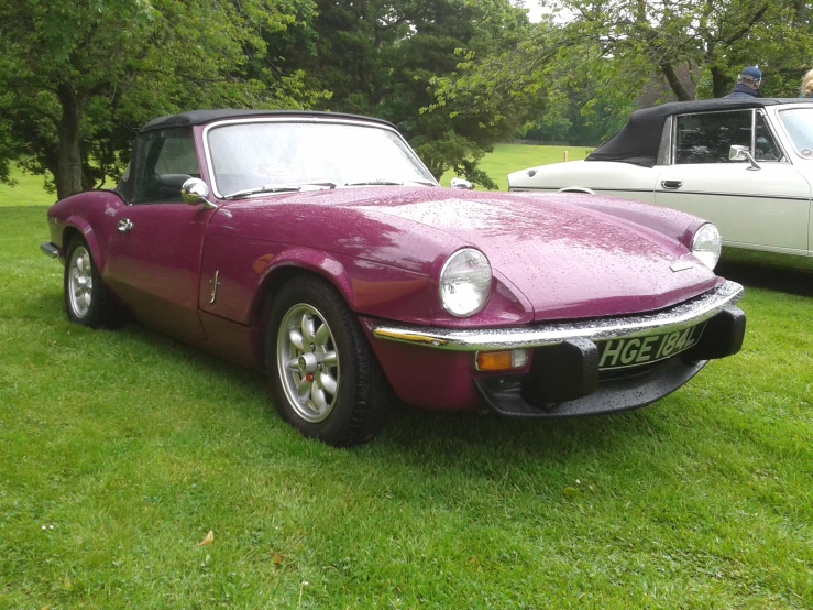 a maroon and black sports car parked in the grass