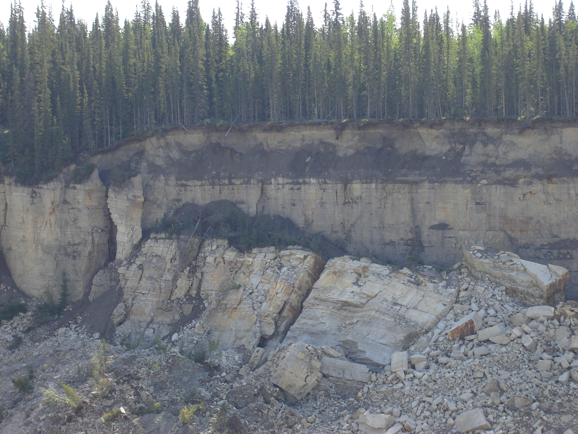 a cliff with rocks is near an area of land that has been eroded into it