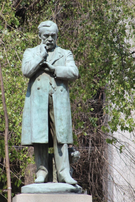 a bronze statue of a man standing next to some bushes