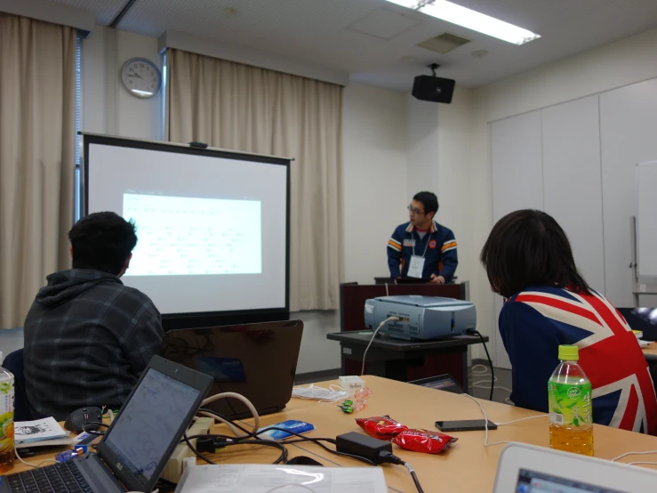 three men in a class room, a man presenting the slide