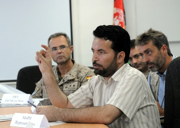 men sit at a meeting table with one pointing