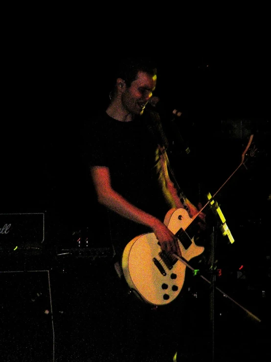 a man standing with a guitar on stage in the dark