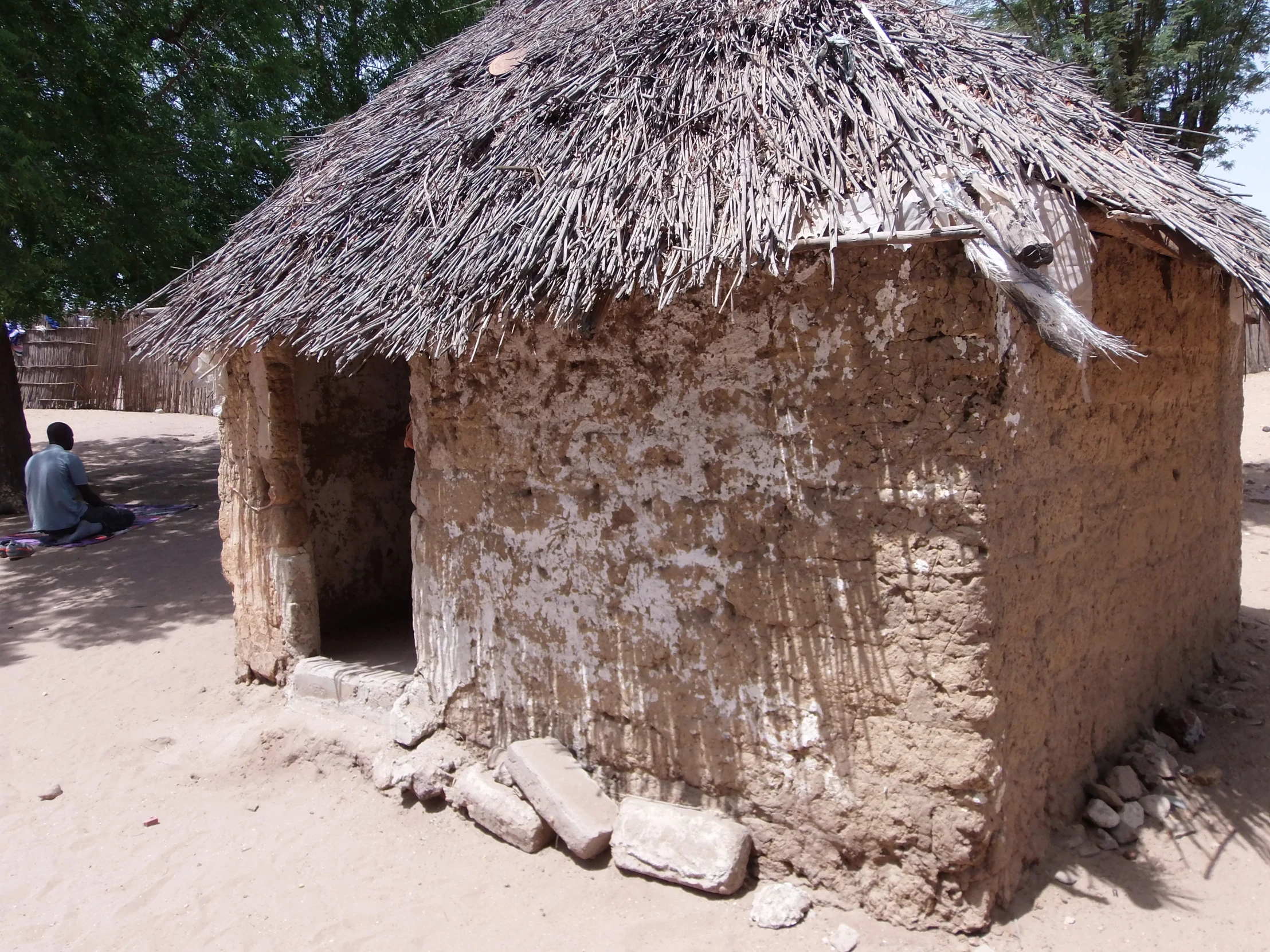 two people sit outside of a house with thatch roof