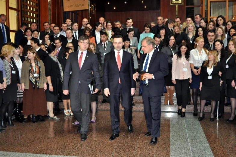 two men in suits and tie standing in front of a crowd