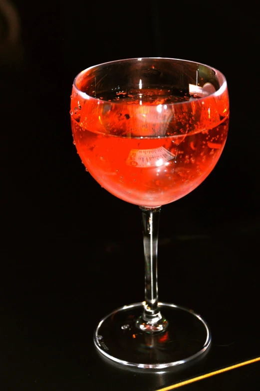 a wine glass filled with red liquid sits on a black table