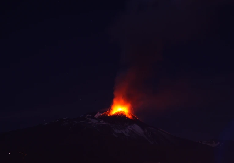 a large volcano with bright red  lava pouring out of the top