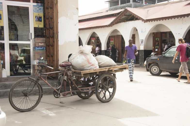 people walking past a store and a bicycle pulling a cart with two bags