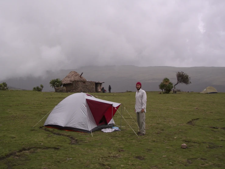 a man standing next to a tent in a field