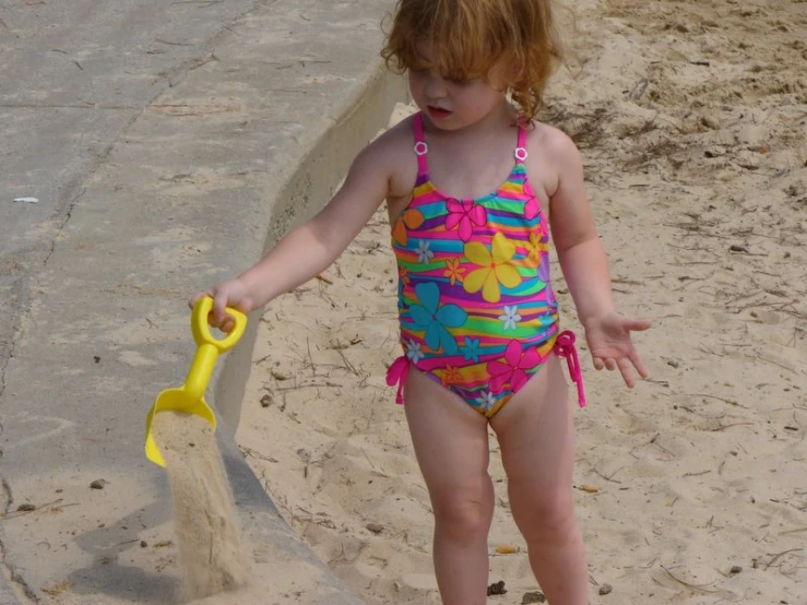 the little girl in her swimsuit playing with the sand