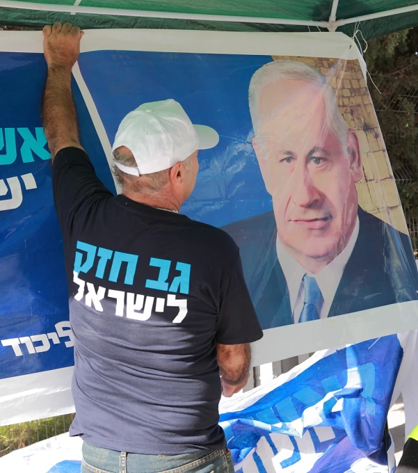 an elderly man placing a portrait of a famous israeli president on a political poster