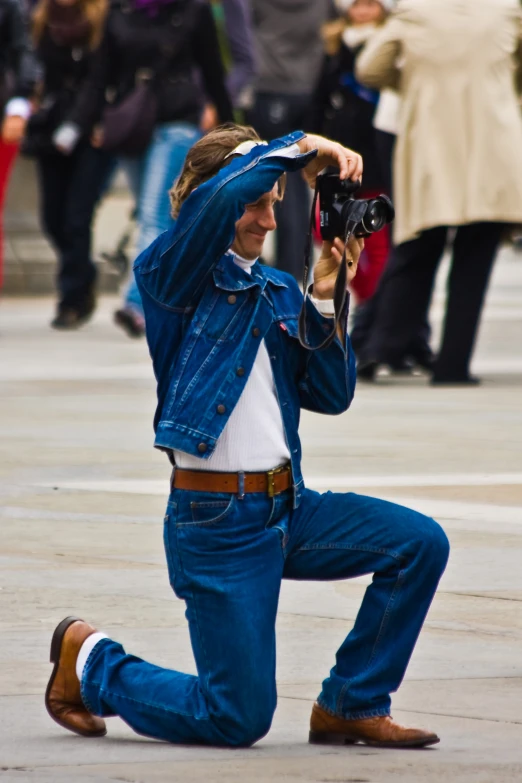 a man in blue jeans with a camera posing