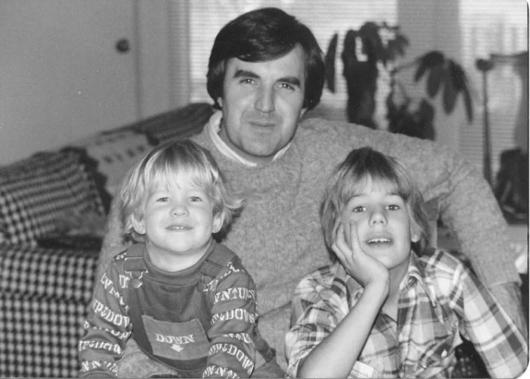 two boys sit in front of their father in the living room