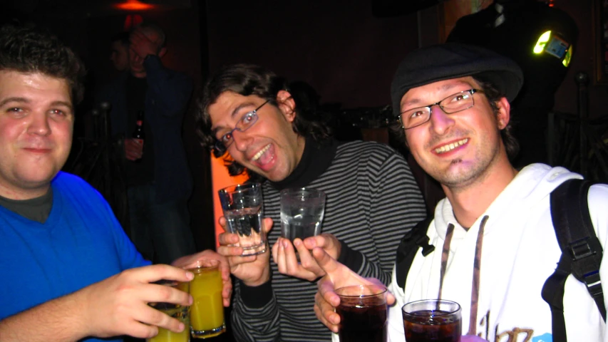 three guys sitting together holding up beers and glasses