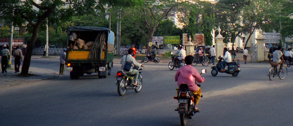 the bicycle riders travel down the street as other vehicles ride behind them