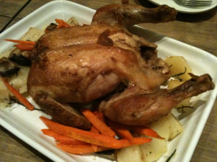 a chicken sits on a white plate with carrots