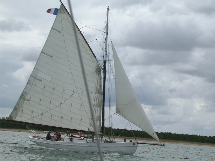 two sail boats ride along the water as people watch