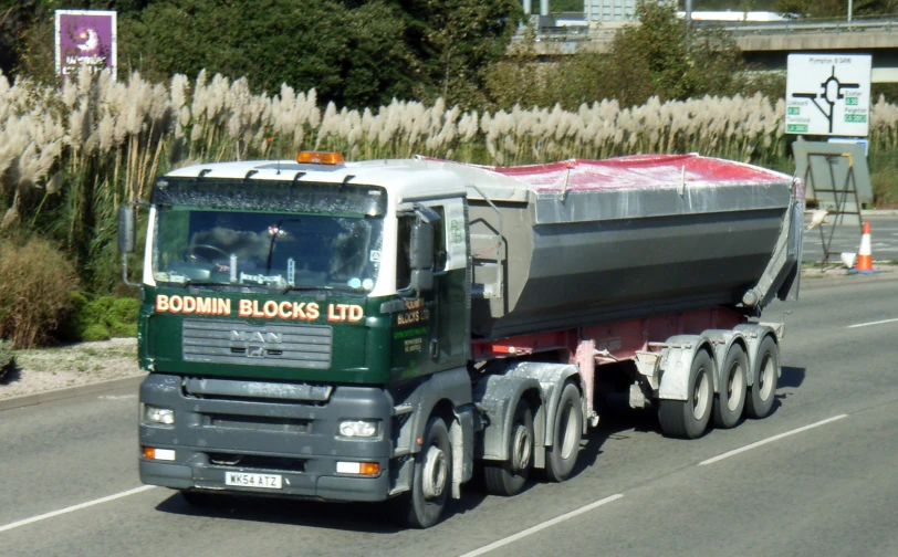 green truck with a large dump behind it on the road