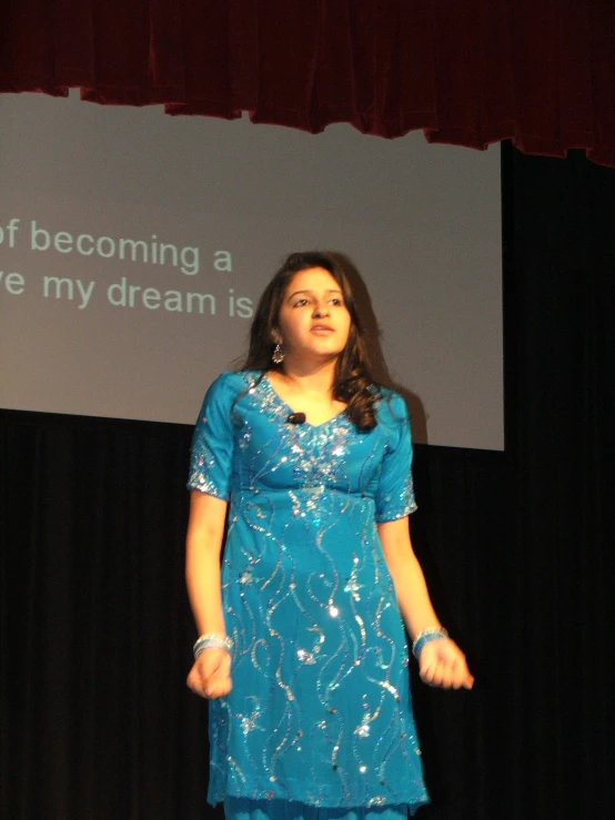 the woman is standing on a stage wearing a bright blue dress