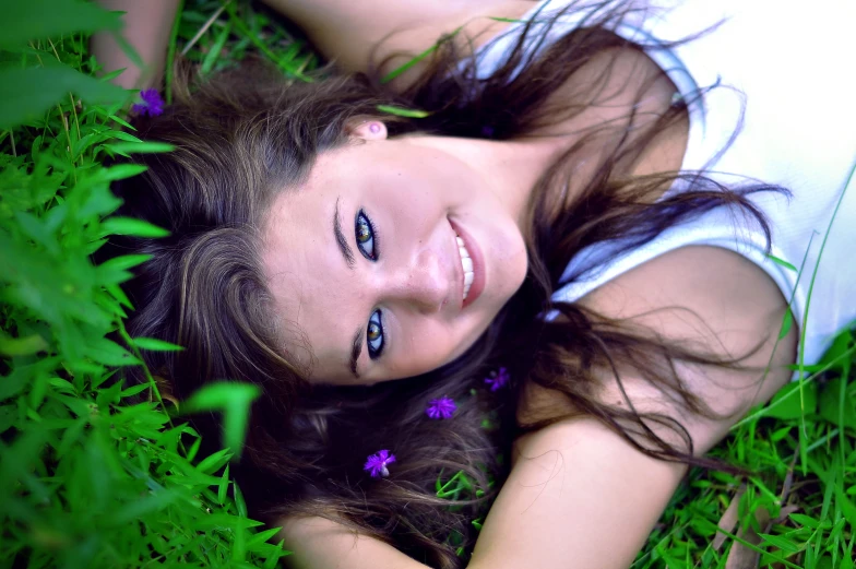 a pretty young woman laying on the grass with purple flowers