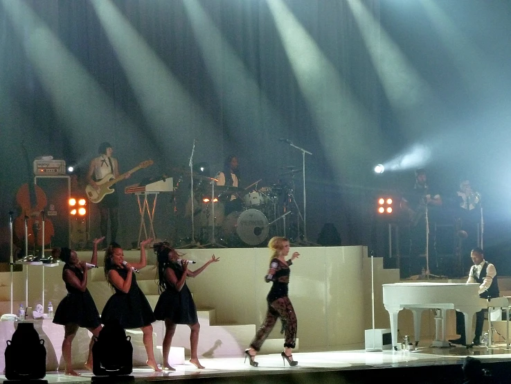 three women standing on stage dancing with two microphones in front of them