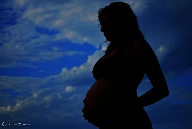 silhouetted pregnant woman against a blue sky with clouds