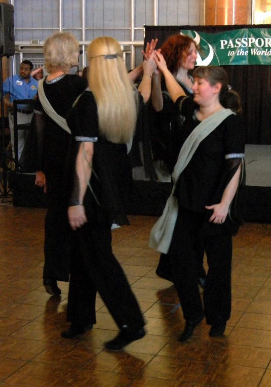 a group of people on a dance floor, one woman wearing long blonde hair and two women in black