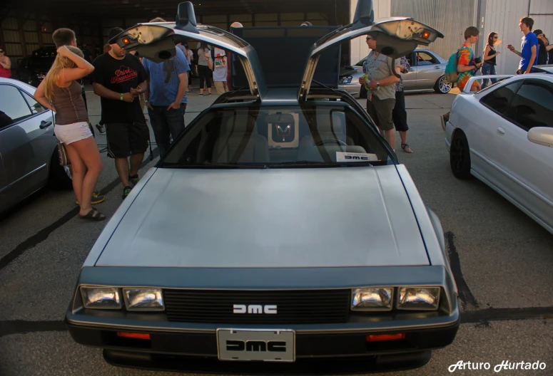 a group of people stand near parked cars with the hood open