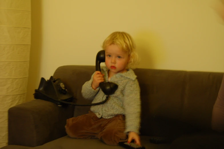 a little girl sitting on a couch holding a telephone