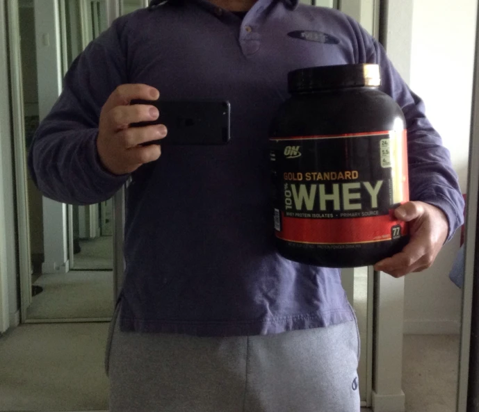 a man standing in front of a mirror holding a bottle of whey