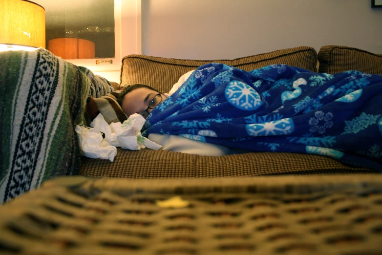 a boy sleeping under blankets on a sofa