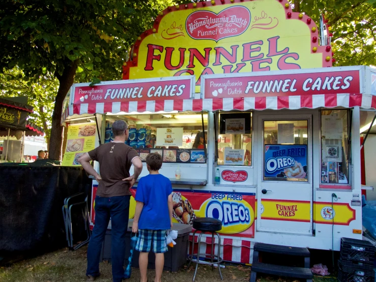 a man and a child standing next to a food stand