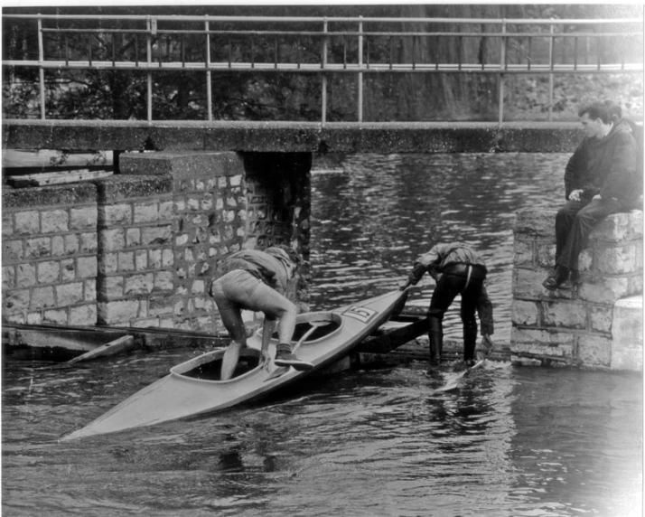 a black and white po of two men putting a boat in to the water