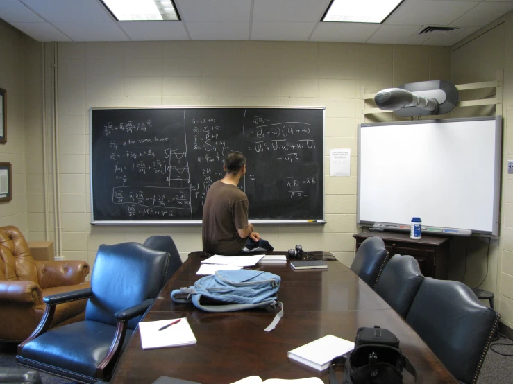 a man in business attire stands near a large board on a blackboard