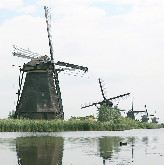 three windmills sit next to the water on a clear day