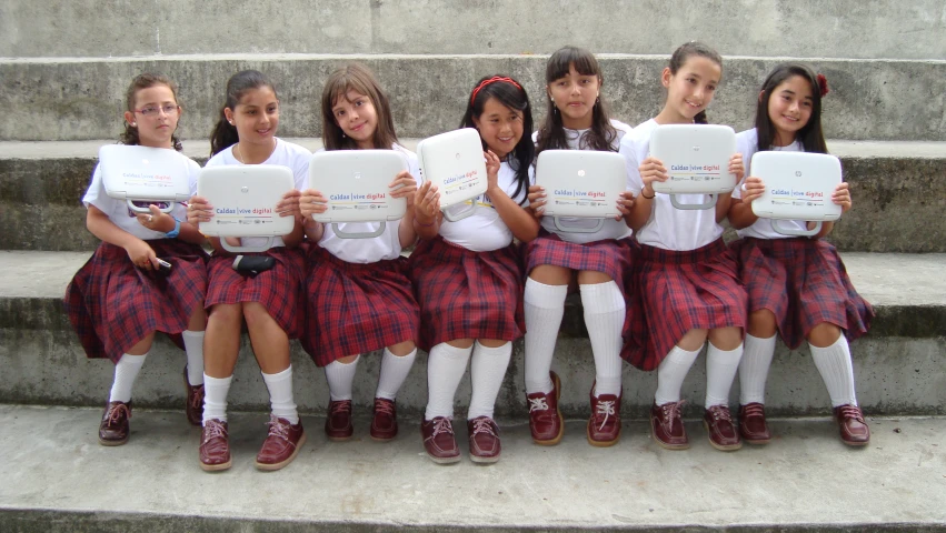 a group of school girls holding laptops while standing on steps