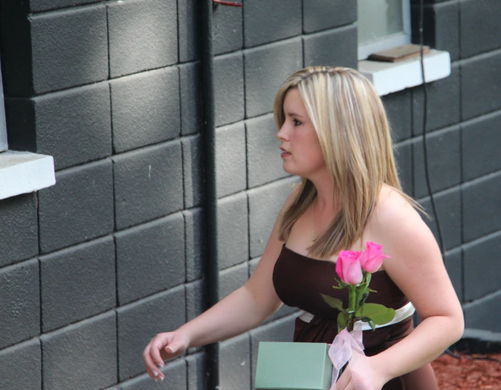 a woman with a pink rose in her hand walking down the street