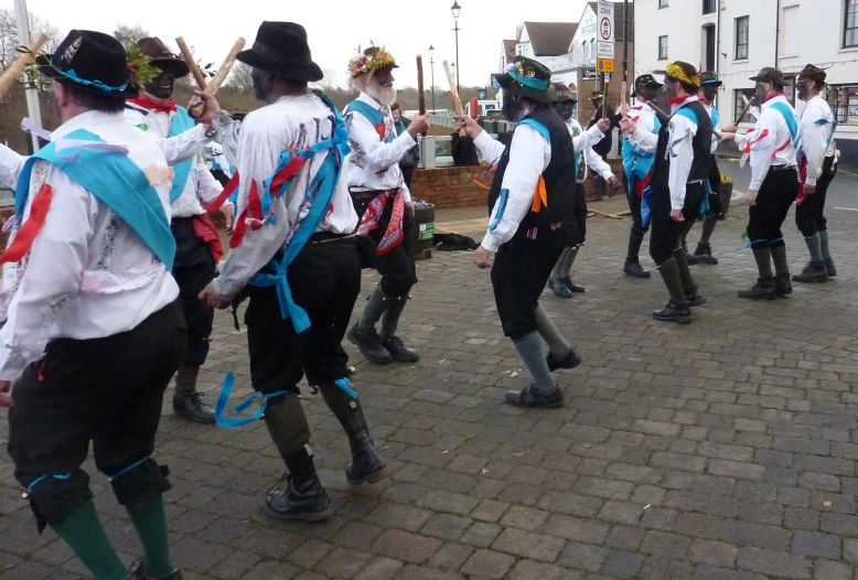 people in costume are dancing with poles and hats