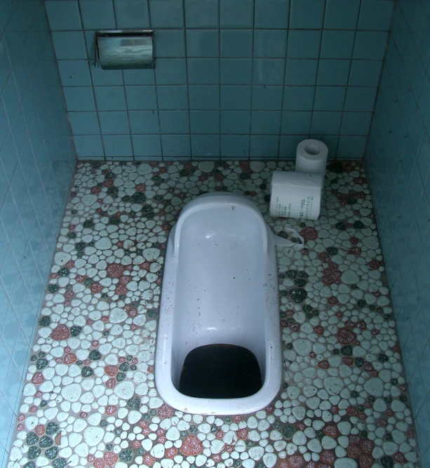 a urinal in a tiled floor bathroom next to toilet paper